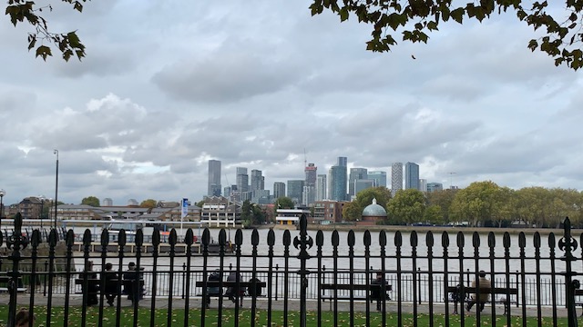 A view across the river to the skyscrapers on the far bank, with black railings and empty benches in front.