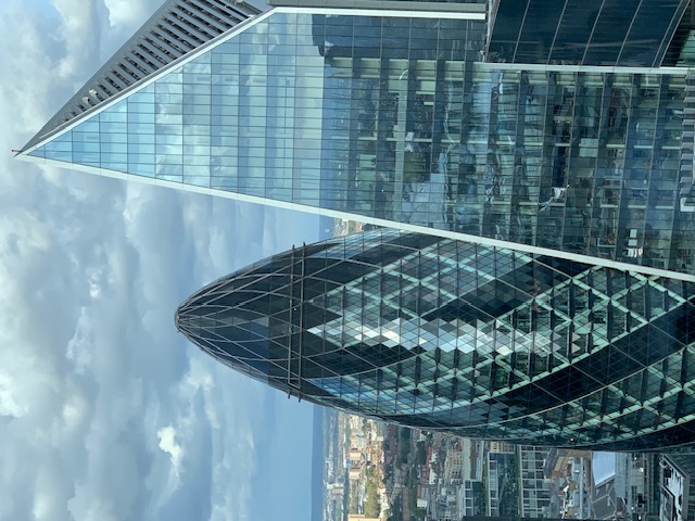 Two glass office towers close up: a rounded one with a diamond pattern beside a sharp, sloping facade.
