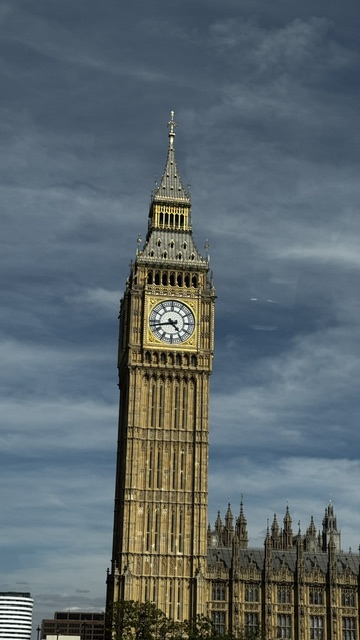 A clock tower with a gilded face against a dark, threatening sky.