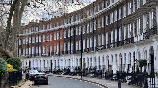 A curved terrace of white and brick townhouses with hotel names above the doors, along a quiet street.