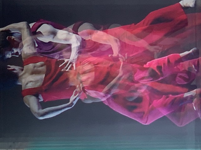 Two dancers in red and pink, photographed in multiple exposure over one another against a dark background.