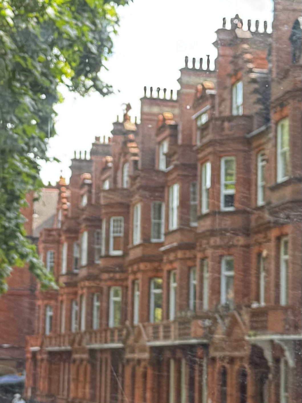 A row of tall brick houses with bay windows and chimneys, photographed out of focus through a window.