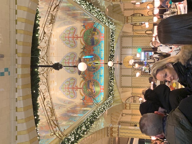 The painted vaulted ceiling of a department store, with Christmas garlands and round lamps above the tables.