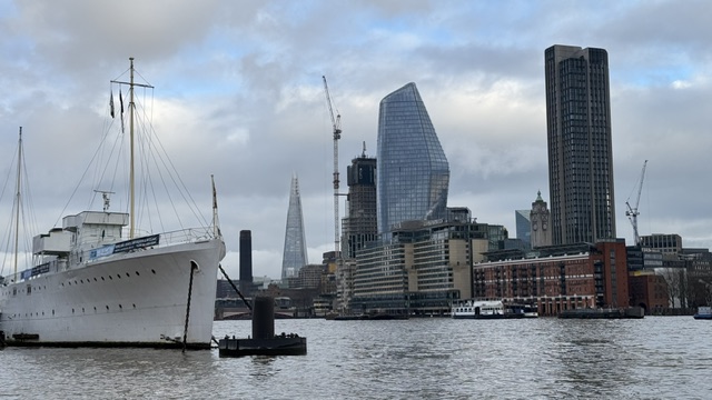 A white ship moored at the quay, with the modern towers of the far bank and construction cranes behind.