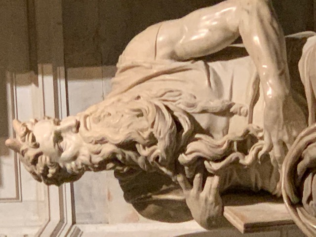 Marble statue of Moses, with an impressively carved beard and muscular arms, in shadow and light.