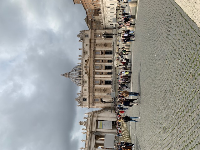 St Peter's Basilica towers over the square while visitors gather under a grey, clouded sky.