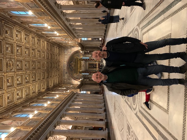 Beneath the gilded ceiling of the Santa Maria Maggiore, between the marble columns and the mosaic pattern of the floor.