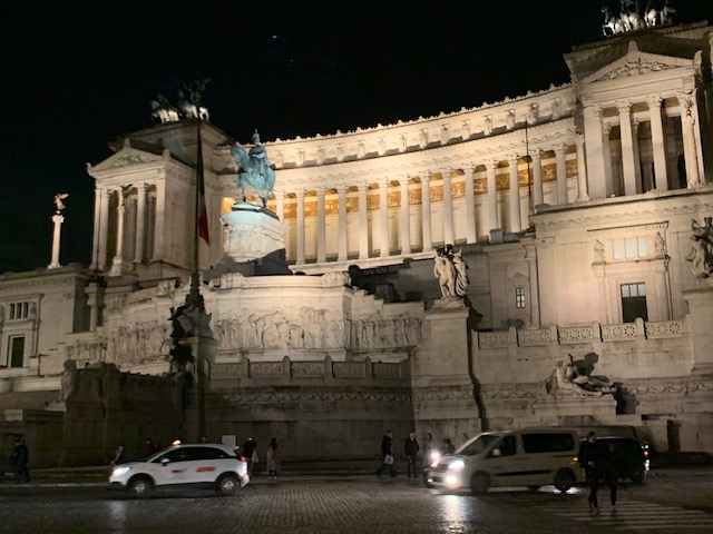 The Vittoriano shines in the evening in illuminated white marble above the busy traffic on the square.