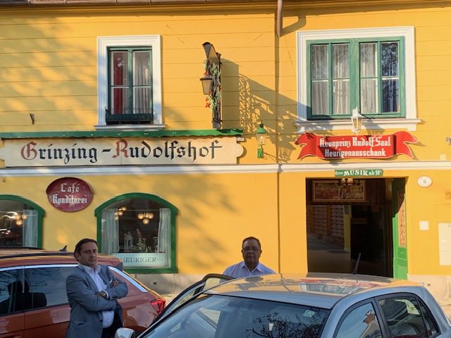 The yellow façade of the Grinzing Rudolfshof Heuriger with green shutters and its painted sign.