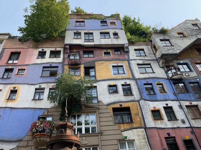 The Hundertwasserhaus seen from below: uneven coloured panels, mismatched windows and trees on the roof.